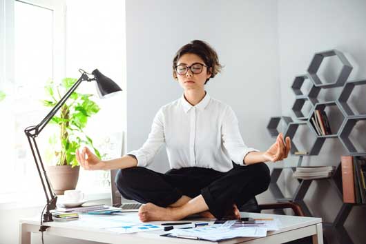 Young beautiful businesswoman meditating on table at workplace in office